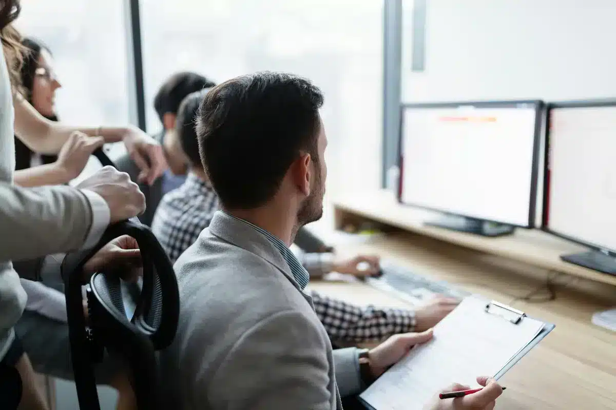 Groupe de collègues en discussion et analyse de données sur ordinateur, illustrant le travail collaboratif pour identifier et prévenir les risques psychosociaux.