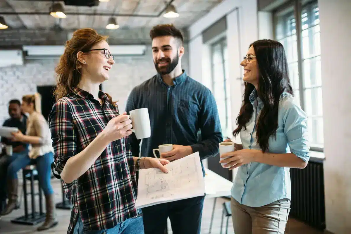 Collègues discutant autour d’un café avec des plans en main, symbolisant un climat organisationnel sain, la collaboration et la mobilisation favorisée par une bonne gestion des risques psychosociaux.