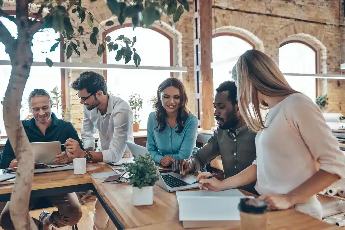 Équipe de travail diversifiée, échangeant autour d’un bureau lumineux, illustrant la collaboration et l’harmonie au sein d’un climat organisationnel sain.